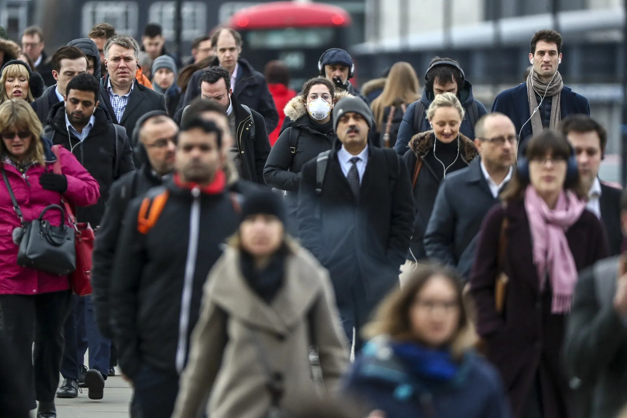 Commuters, including one wearing a protective face mask, walk over London Bridge in London, on Mar. 4.