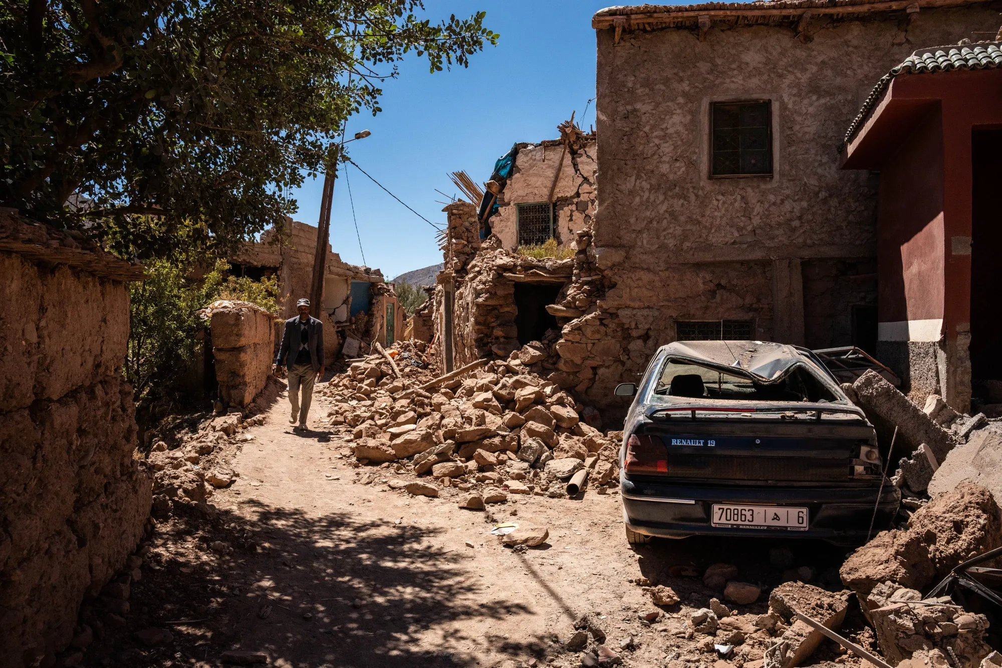A man walks through the streets of the village next to a totally destroyed car, on Sept. 13, 2023 in Tinmel, south of Marrakech, Morocco. 