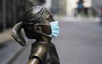 Fearless Girl, a bronze sculpture by Kristen Visbalthe, with a PPE mask on in front of the New York Stock Exchange in the Wall Street Financial District of Manhattan New York May 19, 2020. 
