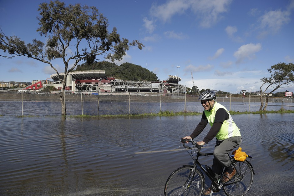 A man rides his bicycle around a flooded section of roadway as demolition continues in the background at Candlestick Park in San Francisco. 