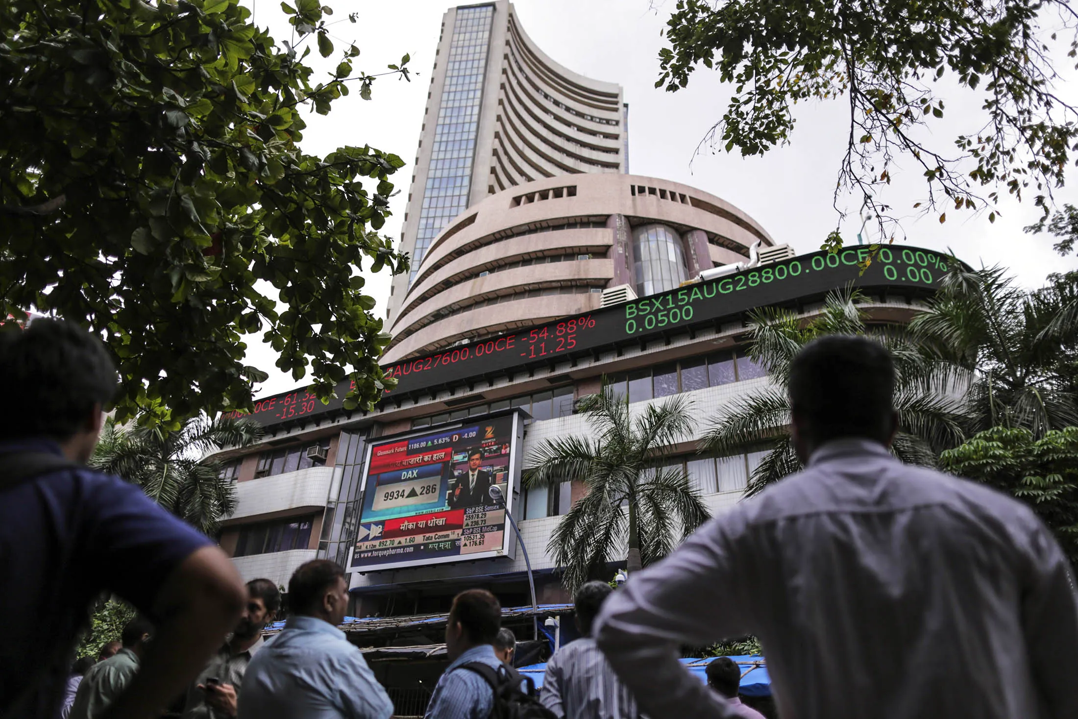 Men look up at an electronic ticker board that indicates stock figures at the Bombay Stock Exchange (BSE) in Mumbai, India, on Tuesday, Aug. 25, 2015. Indian stocks advanced in volatile trading a day after the benchmark gauge plunged the most in six years, as banks helped counter declines in software exporters.
