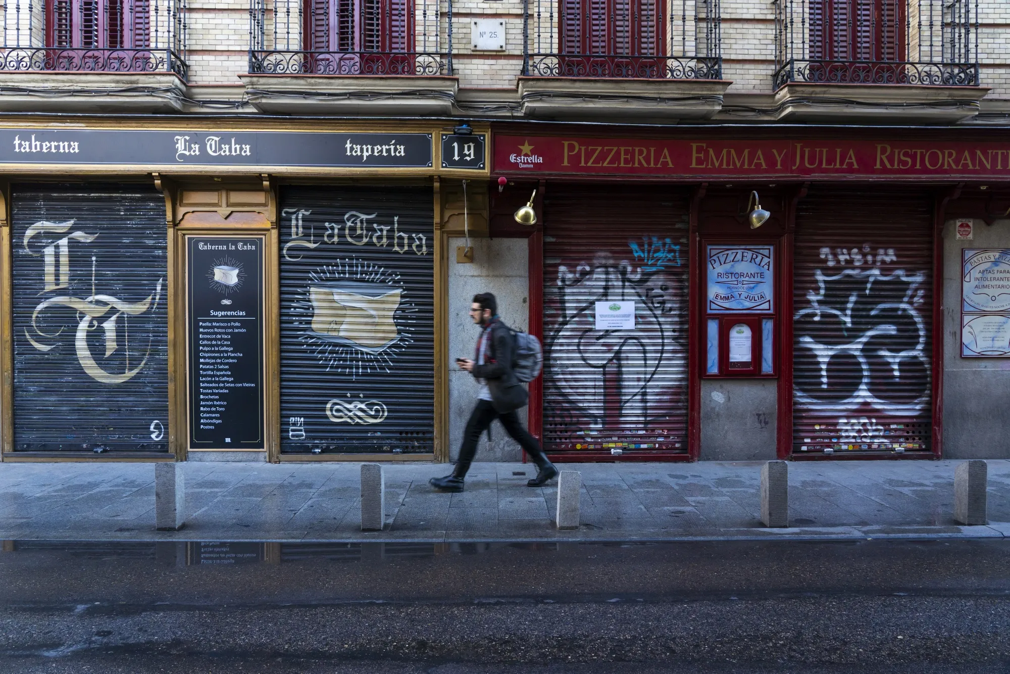A pedestrian walks past a closed tapas bar, left, and restaurant in Madrid.
