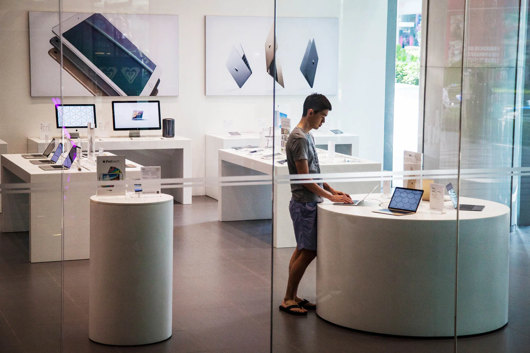 A shopper tries out an Apple Inc. Macbook laptop computer inside an iStudio store in the Orchard Central shopping mall on Orchard Road in Singapore, on Sunday, June 21, 2015. Consumer prices prices declined for a sixth straight month in April and employment contracted last quarter for the first time since 2009.
