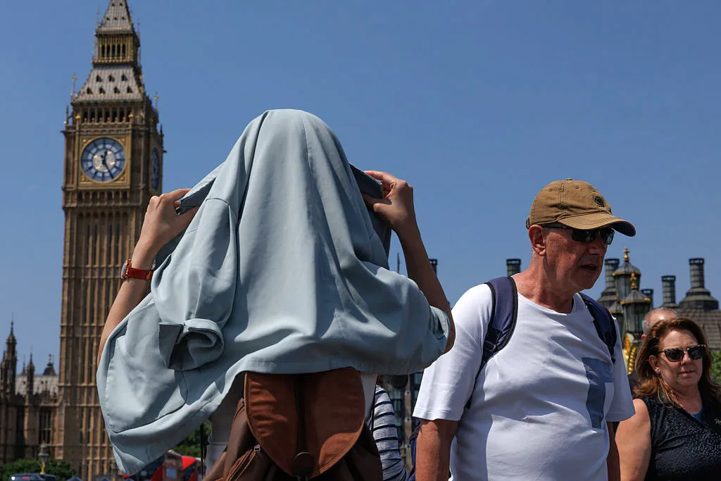 A woman covers her head from the sun on Westminster Bridge.