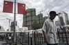 A pedestrian walks past Chinese national flags hanging on a street light as residential buildings stand under construction in the background in Shanghai, China.