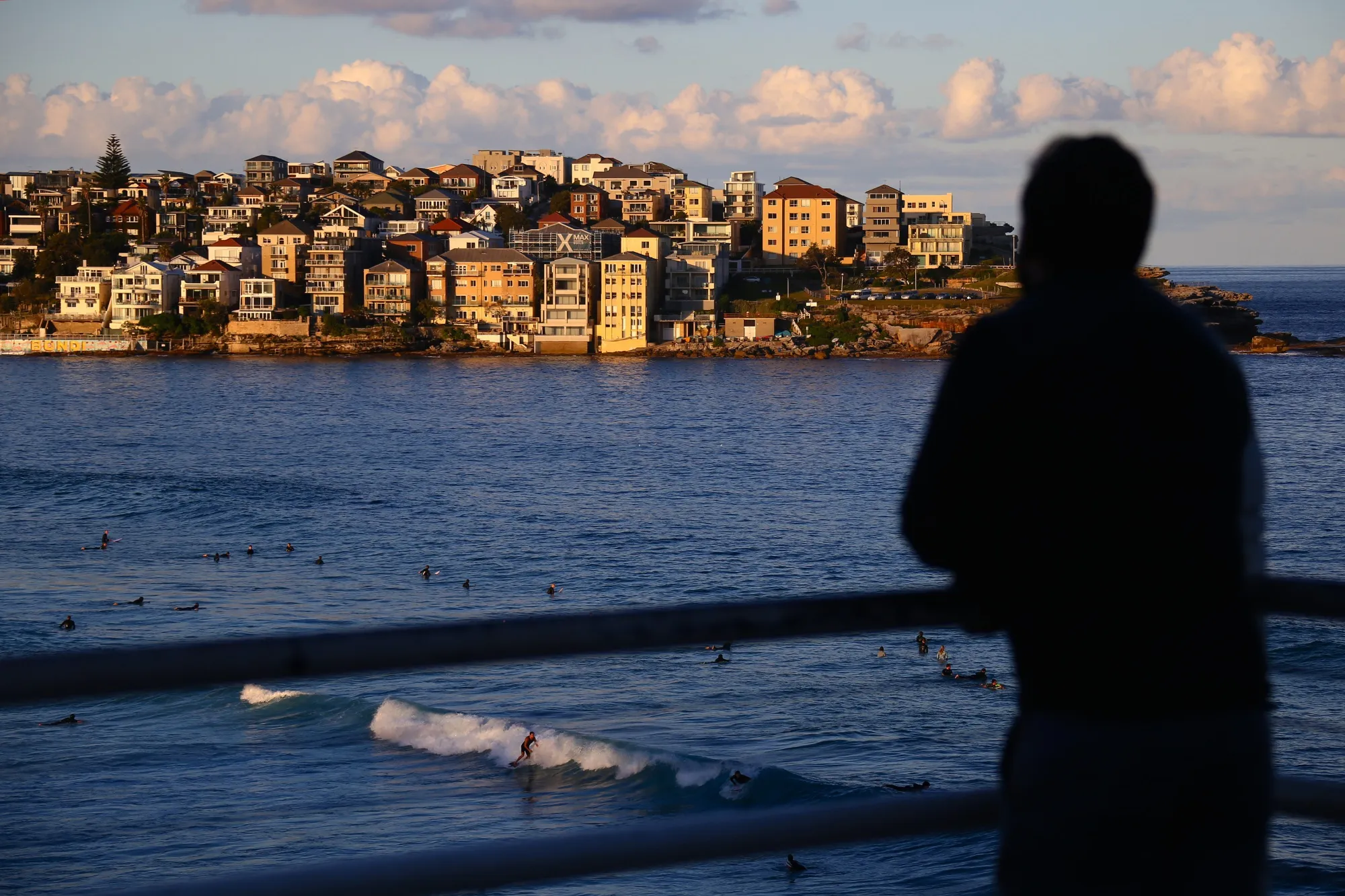 A man is silhouetted as he looks out at surfers at Bondi Beach as residential buildings stand in the background in Sydney, Australia.