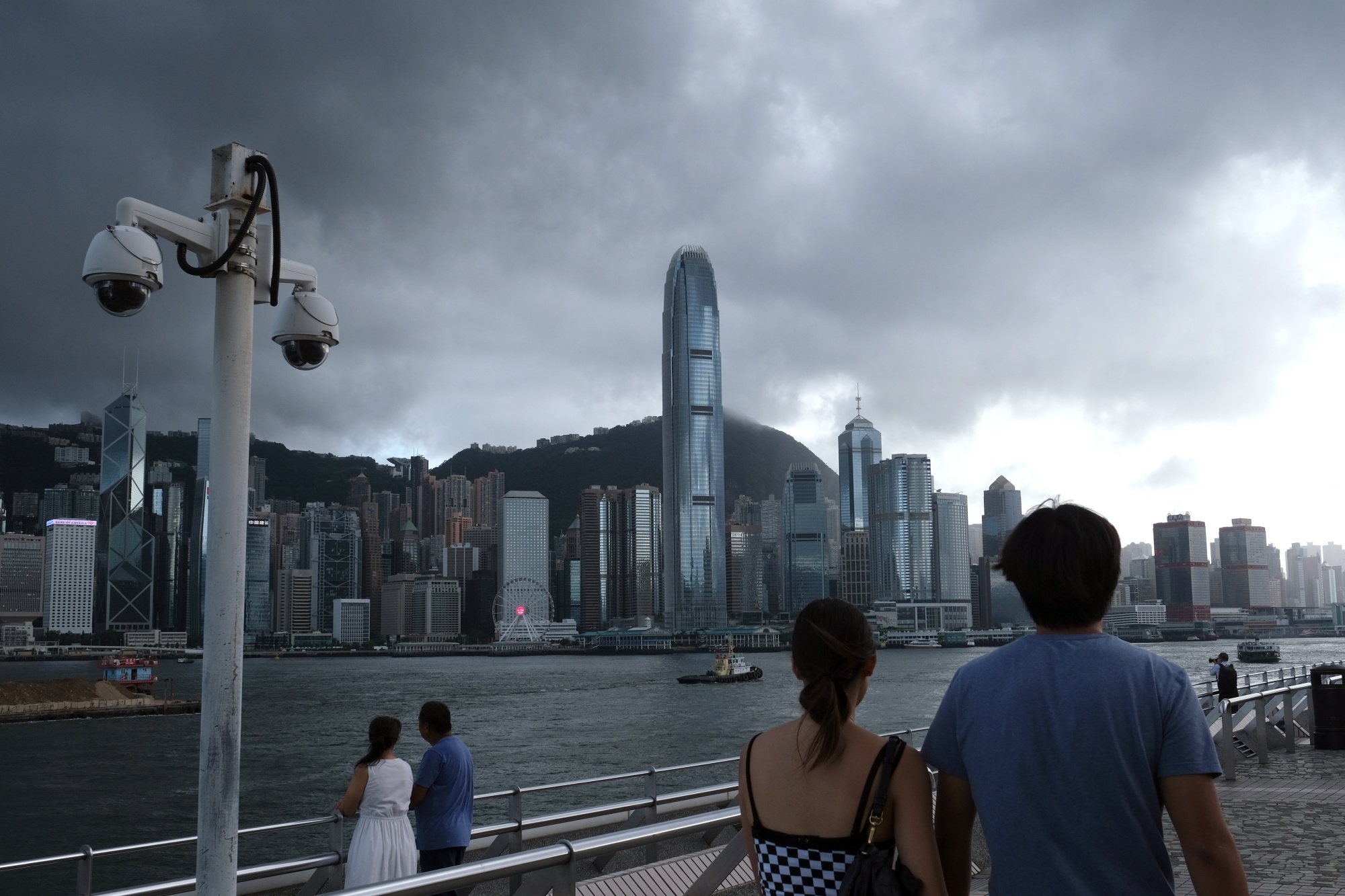 Pedestrians walk past a pair of security cameras along the Tsim Sha Tsui waterfront as buildings stand across Victoria Harbor in Hong Kong, on&nbsp;July 7.