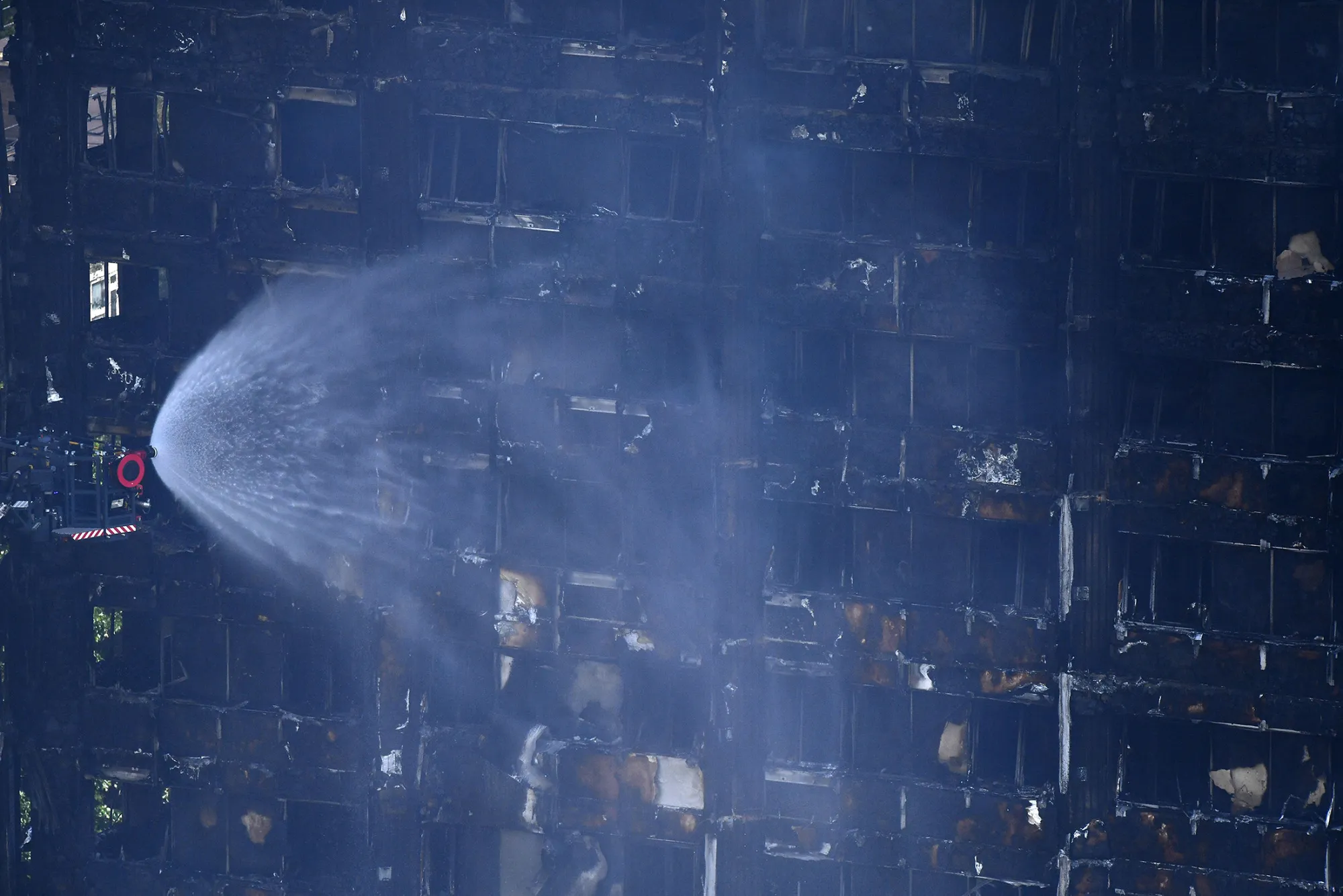Firemen spray water onto the facade of the Grenfell Tower after a fire ripped through the building in west London on June 14, 2017.At least six people were killed Wednesday when a massive fire tore through a London apartment block overnight, with survivors voicing anger over longstanding safety fears at the 24-storey Grenfell Tower. / AFP PHOTO / Ben STANSALL        (Photo credit should read BEN STANSALL/AFP/Getty Images)