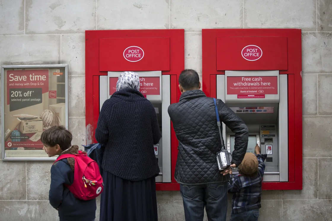 Customers use an ATM outside a post office in London.