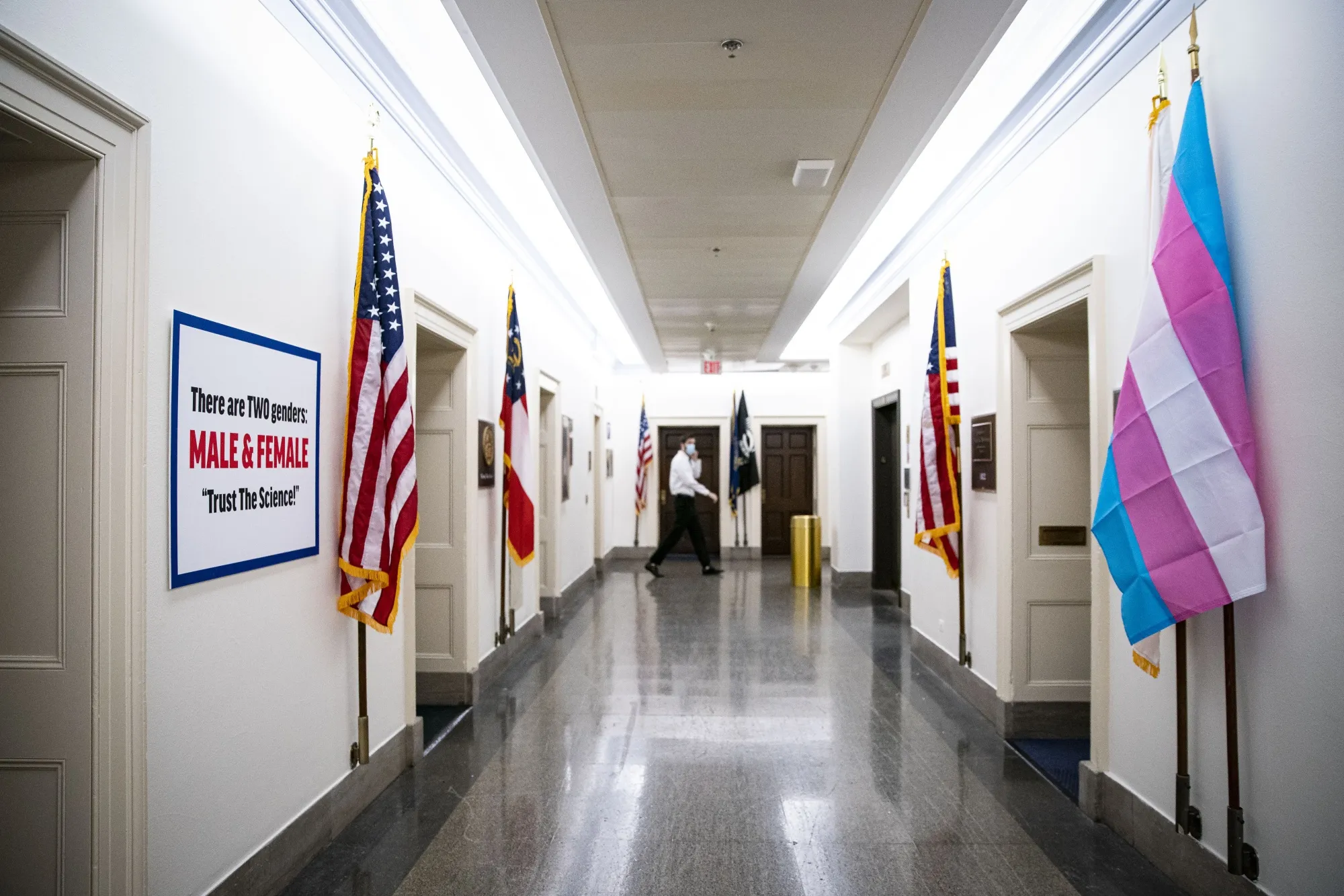 A sign hangs on the wall outside the office of Rep. Marjorie Taylor Greene (R-GA) as a Transgender Pride flag hangs outside the office of Rep. Marie Newman (D-IL) (R) on Capitol Hill.