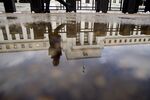 A woman walks past the Marriner S. Eccles Federal Reserve building as it is reflected in a puddle of water in Washington, D.C., U.S., on Tuesday, Jan. 27, 2015. 