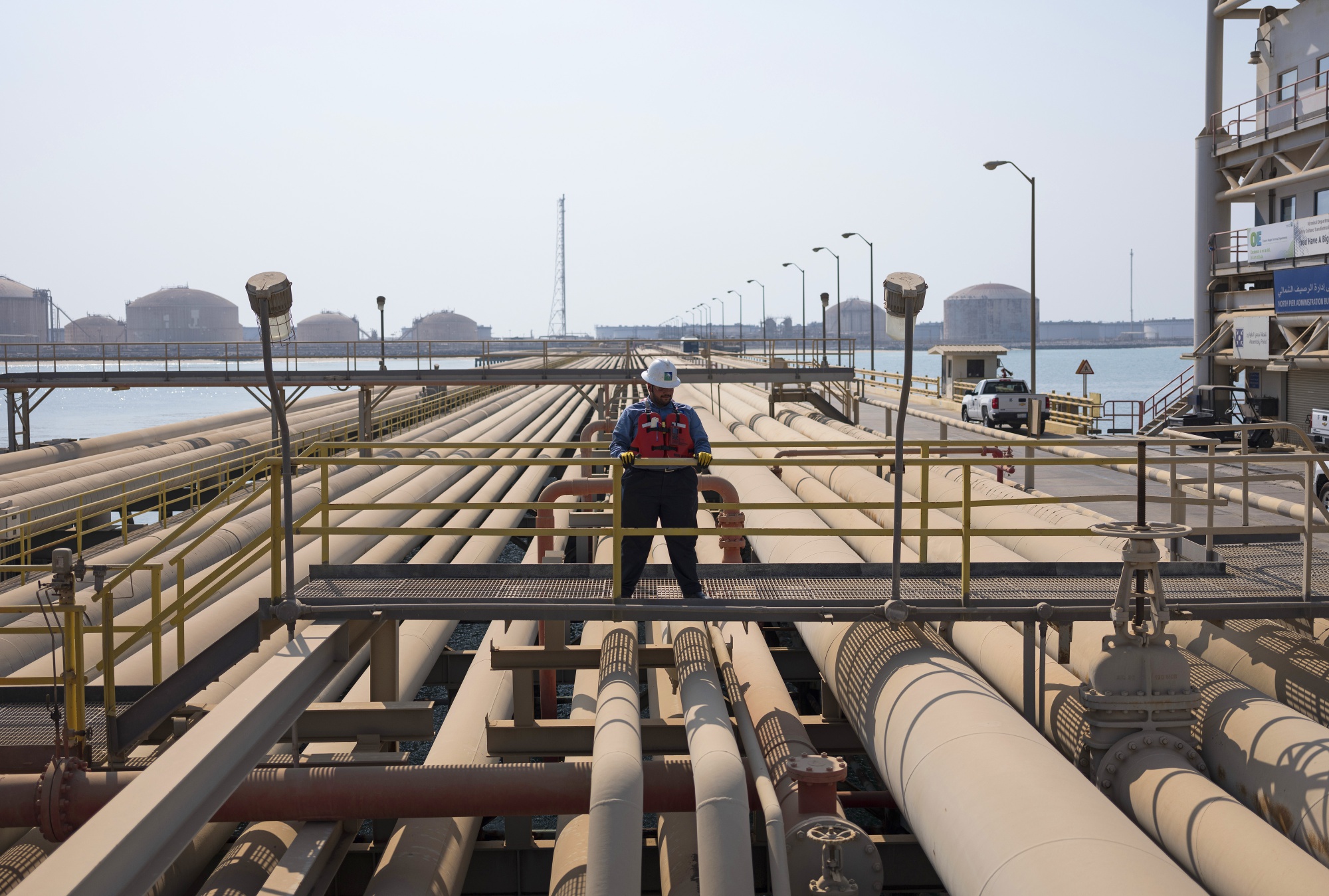 An employee looks out across oil pipes at the North Pier Terminal, operated by Saudi Aramco, in Ras Tanura, Saudi Arabia.