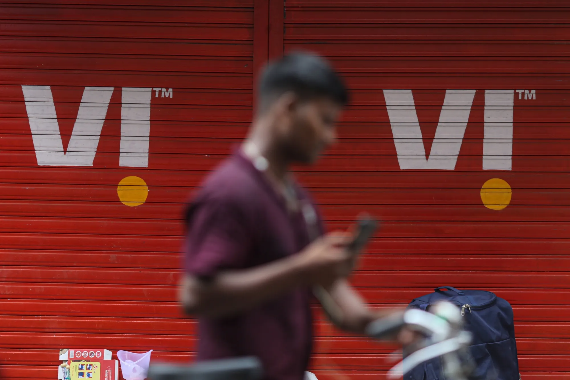 A pedestrian with a mobile phone walks past a sign for Vodafone Idea Ltd. in Mumbai.