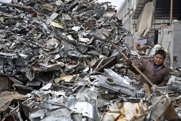 A worker shovels scrap metal onto the back of a truck near W