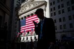 A pedestrian views a mobile device while walking past an American flag displayed outside of the New York Stock Exchange (NYSE) in New York, U.S., on Monday, July 3, 2017. U.S. stocks rose in light trading and the dollar strengthened as factory data bolstered optimism in the strength of the American economy. Crude climbed for an eighth day.

