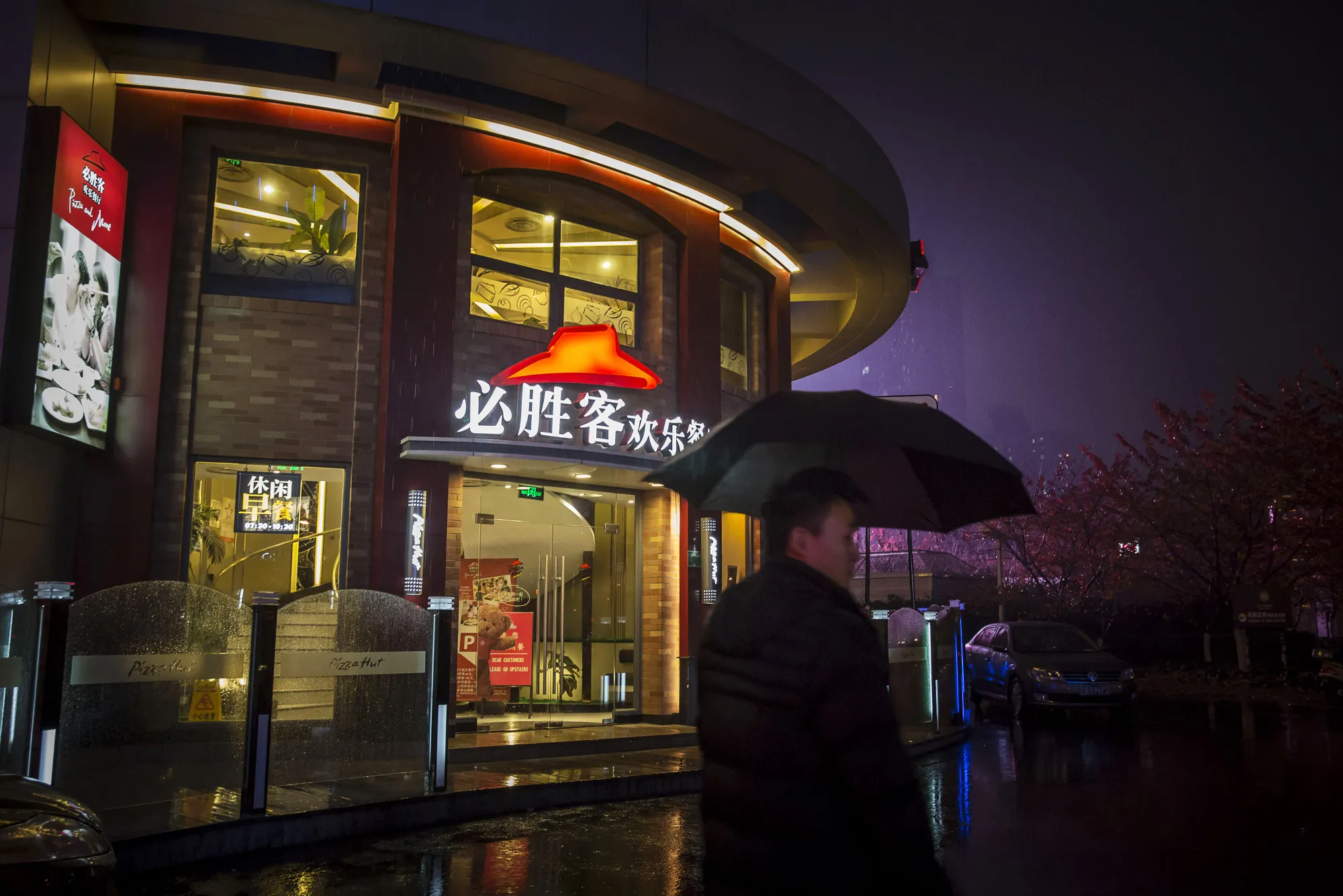 A pedestrian&nbsp;walks&nbsp;past a Yum! Brands Inc. Pizza Hut restaurant at night in Shanghai.