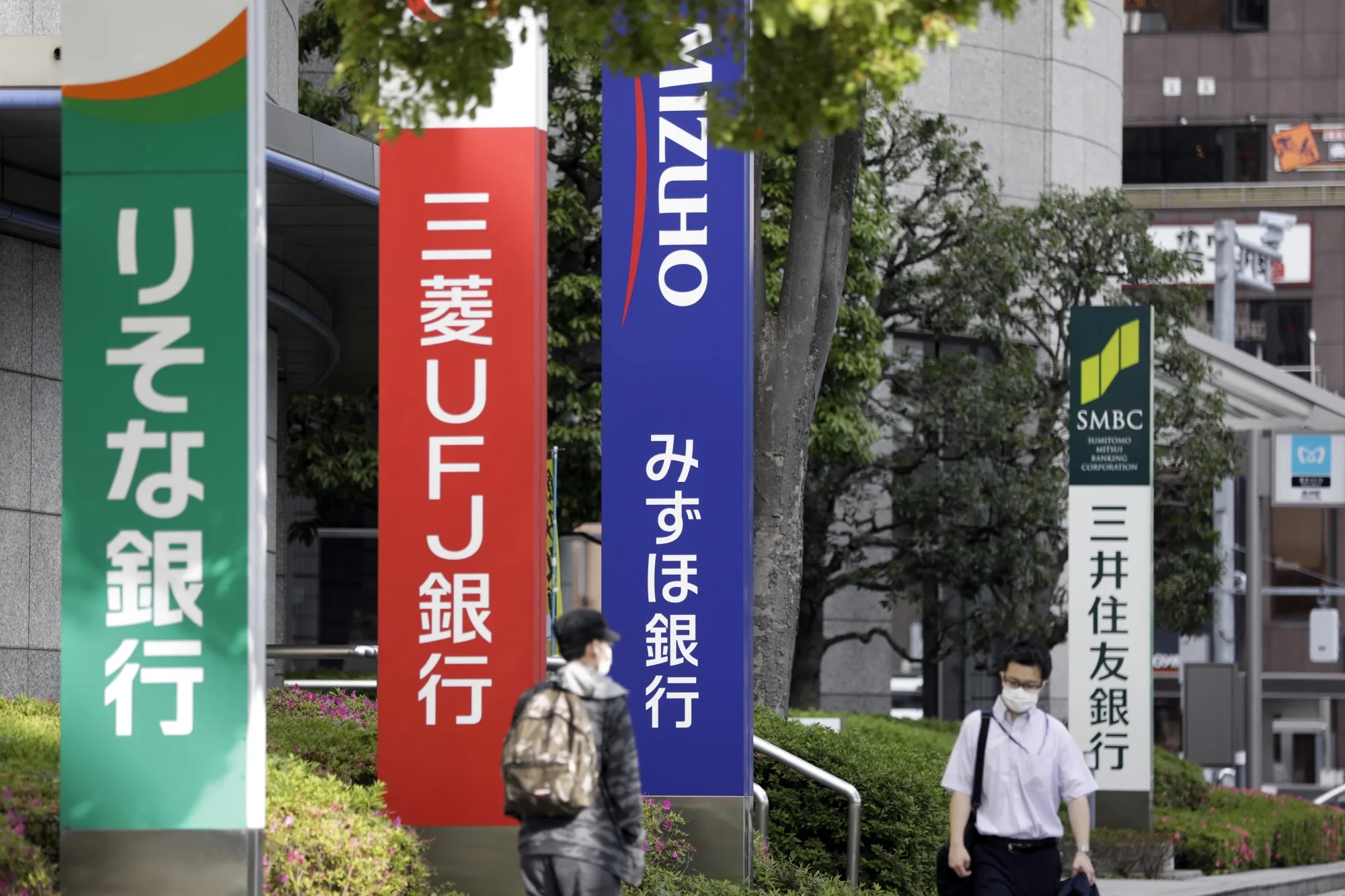 Pedestrians wearing protective masks walk past signage for Resona Bank Ltd., from left, MUFG Bank Ltd., Mizuho Bank Ltd. and Sumitomo Mitsui Banking Corp. in Tokyo, on May 13.