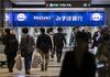 Pedestrians walk in front of Mizuho Bank Ltd. automated teller machines (ATMs).