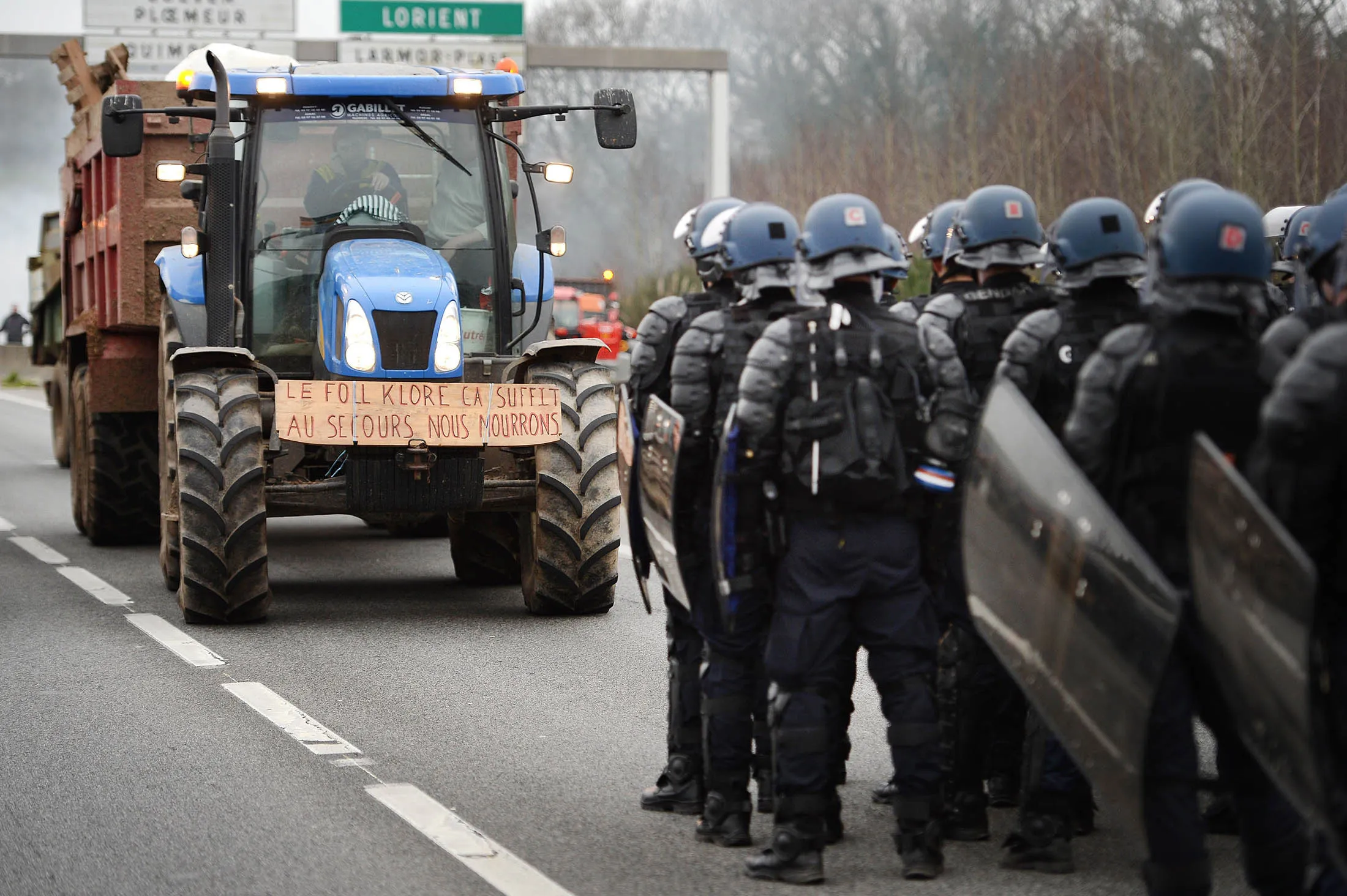 French gendarmes stand on the RN 165 motorway facing protesters in a tractor bearing a sign reading 'Enough with Le Foll klore, help we are dying' (in reference to French Agriculture minister Stephane Le Foll) as farmers block the motorway access to Lorient, western France, on Jan. 25.
