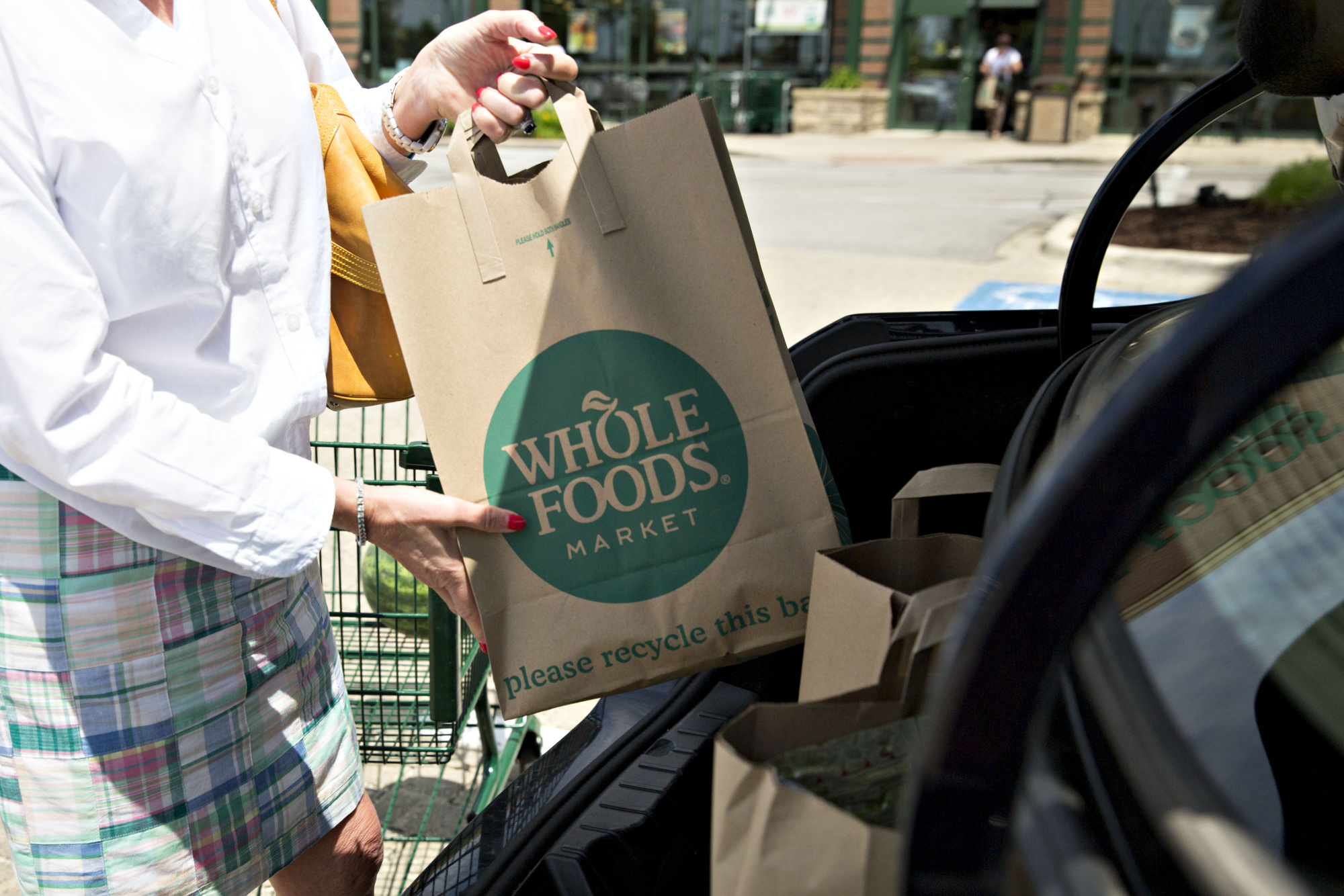 A customer loads shopping bags into a vehicle outside a Whole Foods Market Inc. location in Naperville, Illinois, U.S., on Friday, June 16, 2017. Amazon.com Inc. will acquire Whole Foods Market Inc. for $13.7 billion, a bombshell of a deal that catapults the e-commerce giant into hundreds of physical stores and fulfills a long-held goal of selling more groceries.