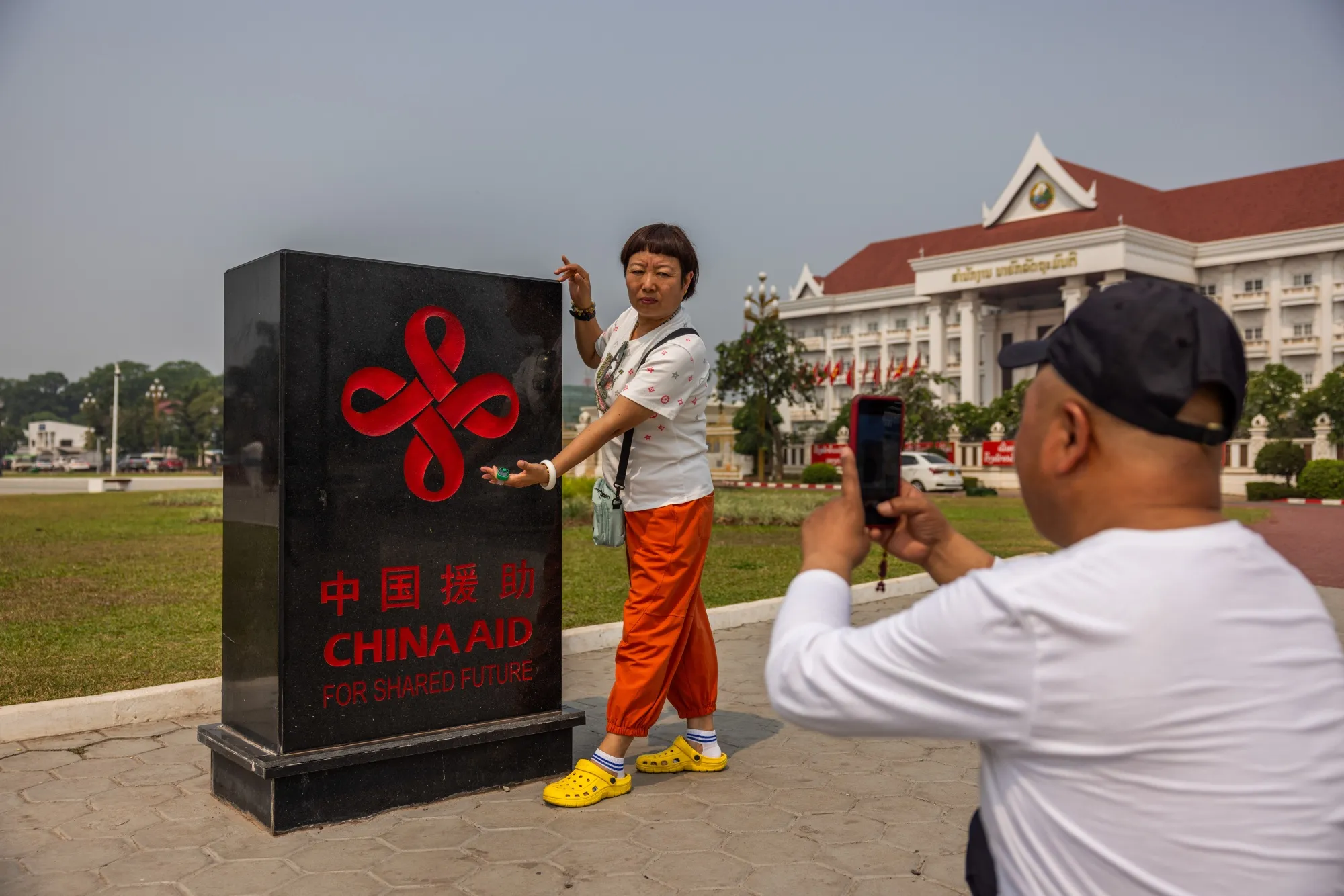 Tourists pose for&nbsp;photos with a China Aid plaque at the Patuxay Victory Monument in Vientiane.