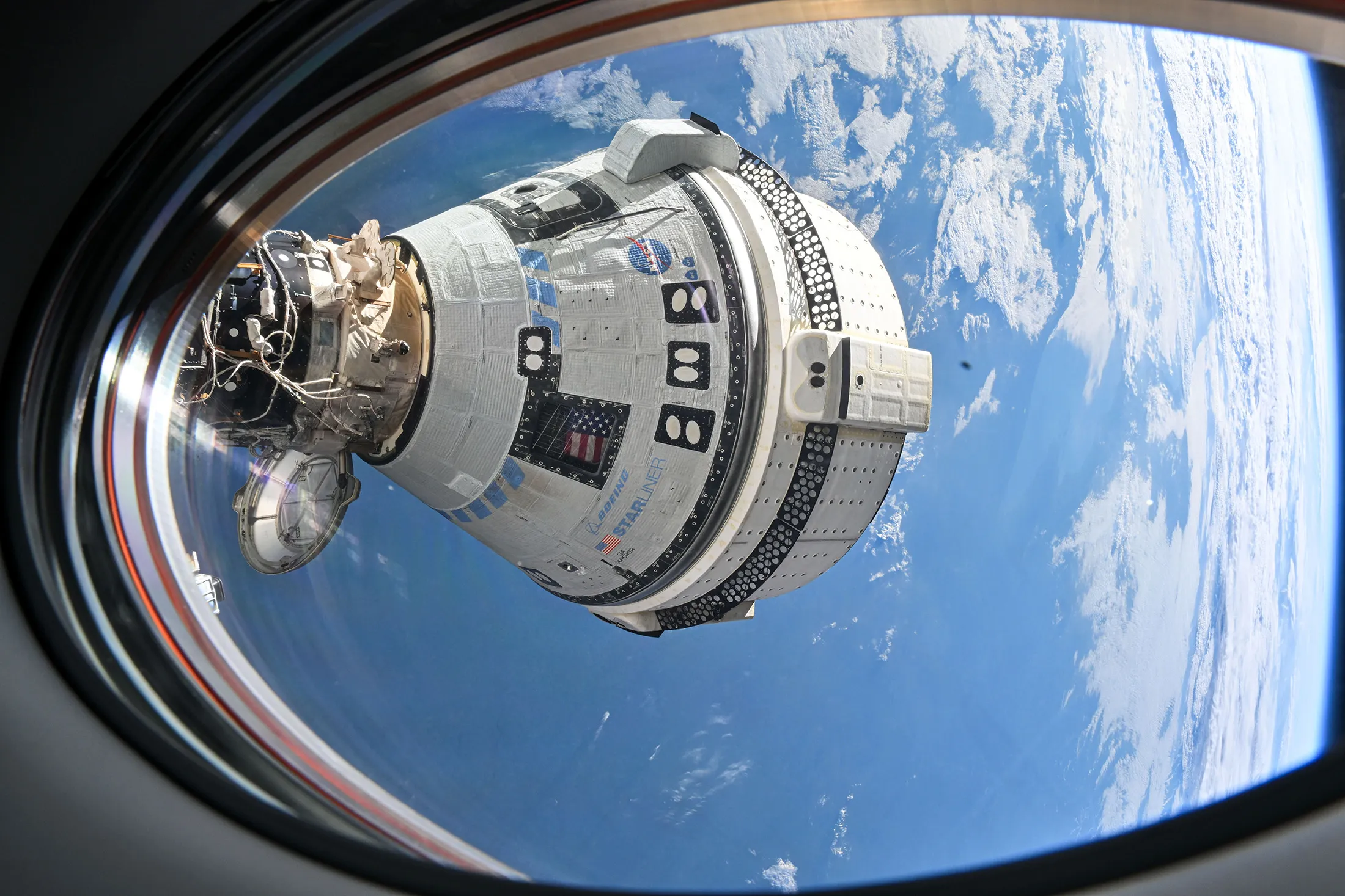 Boeing’s Starliner spacecraft docked to the International Space Station, as seen from a window on SpaceX’s Dragon spacecraft.