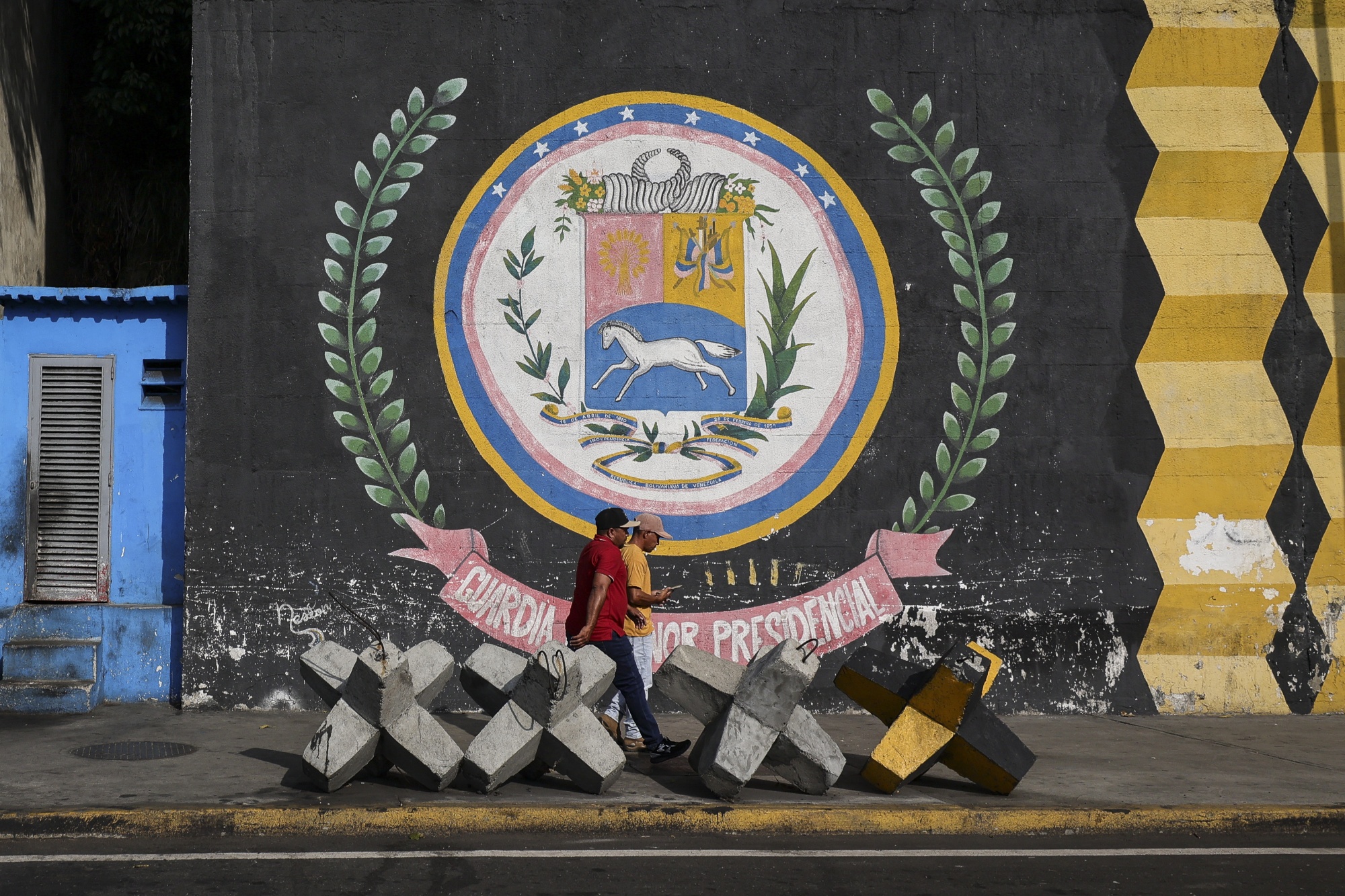 People walk in front of a mural painted with the Venezuelan coat of arms after the capture of Nicolas Maduro by US forces on Jan. 7, 2026 in Caracas, Venezuela.