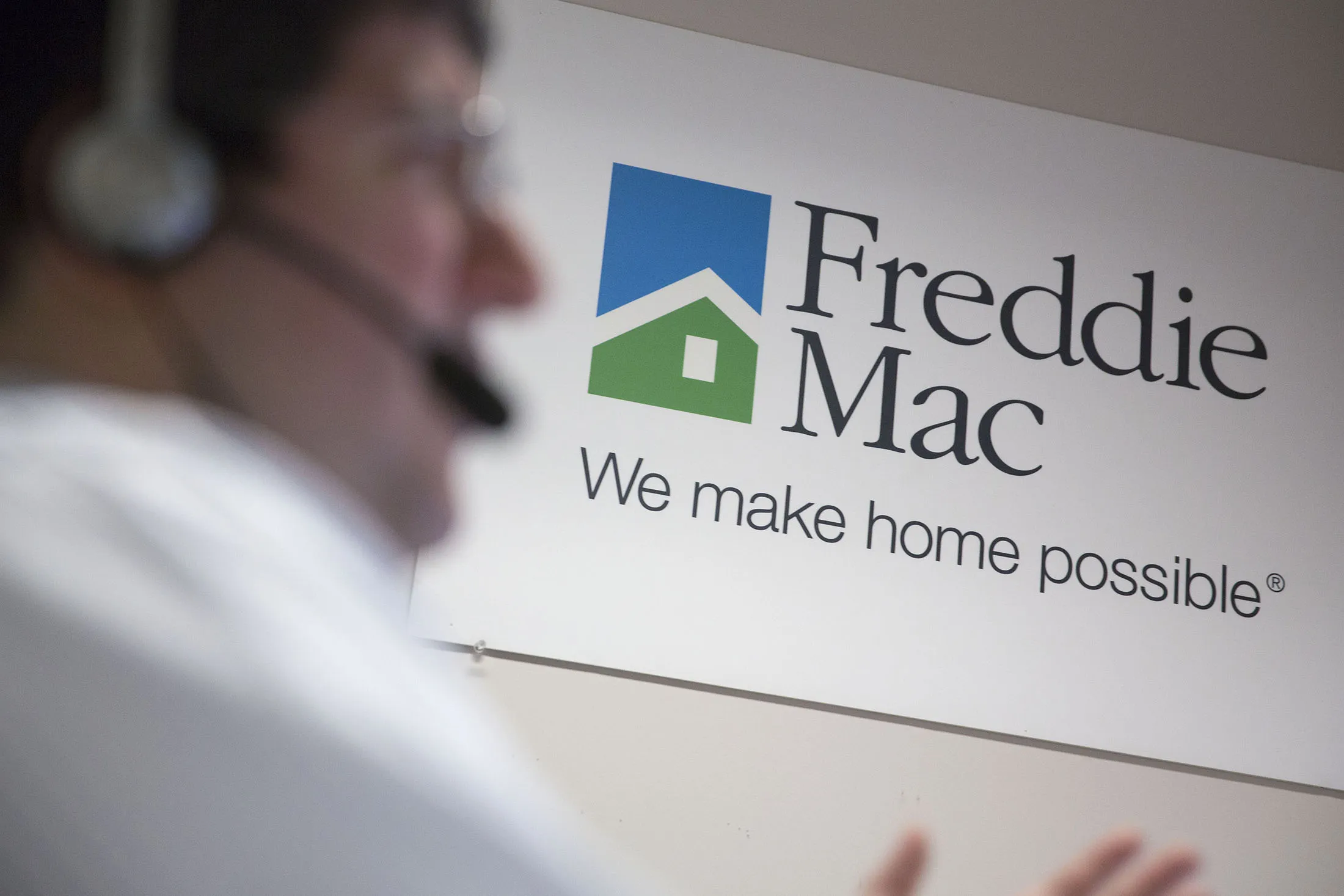 A Freddie Mac sign hangs behind employee John Estrada as he works in the borrower contact unit area at Freddie headquarters in McLean, Virginia, U.S., on Tuesday, April 8, 2014. Senator Sherrod Brown, an Ohio Democrat and a member of the Senate Banking Committee, said a bipartisan bill to replace Fannie Mae and Freddie Mac is too complicated and doesn't do enough to address too-big-to-fail concerns or provide assistance for affordable housing. The panel will consider the measure on April 29.
