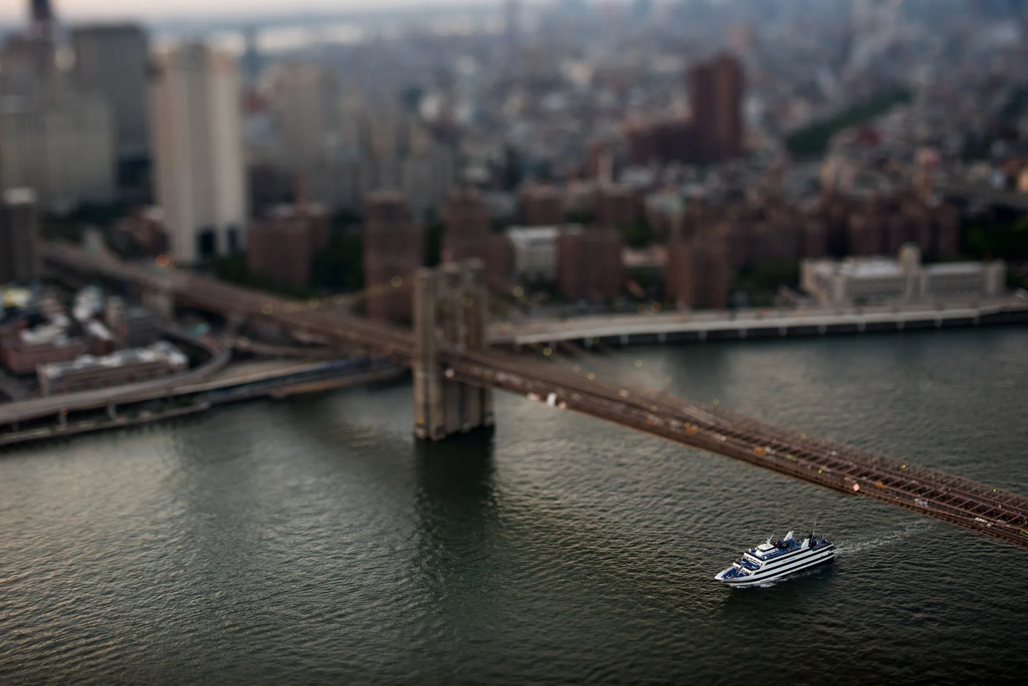 A boat passes beneath the Brooklyn Bridge at dusk in this aerial photograph taken with a tilt-shift lens above New York, U.S., on Friday, June 19, 2015. The Standard &amp; Poor's 500 Index fell, with the gauge dropping below its price for the past 50 days, while Treasuries retreated.
