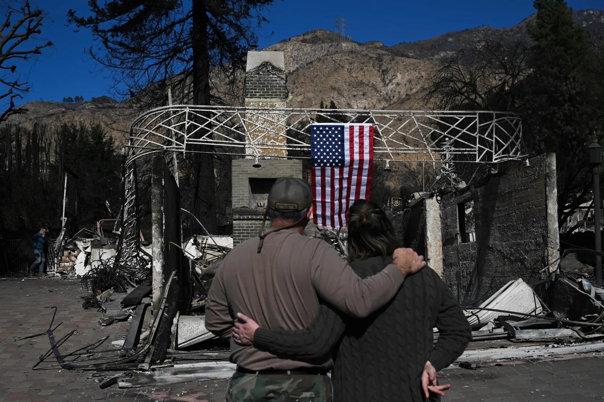 Altadena homeowners Brian McMahon (left) and Emily Philips (right) survey what’s left of their house on Jan. 13, 2025.