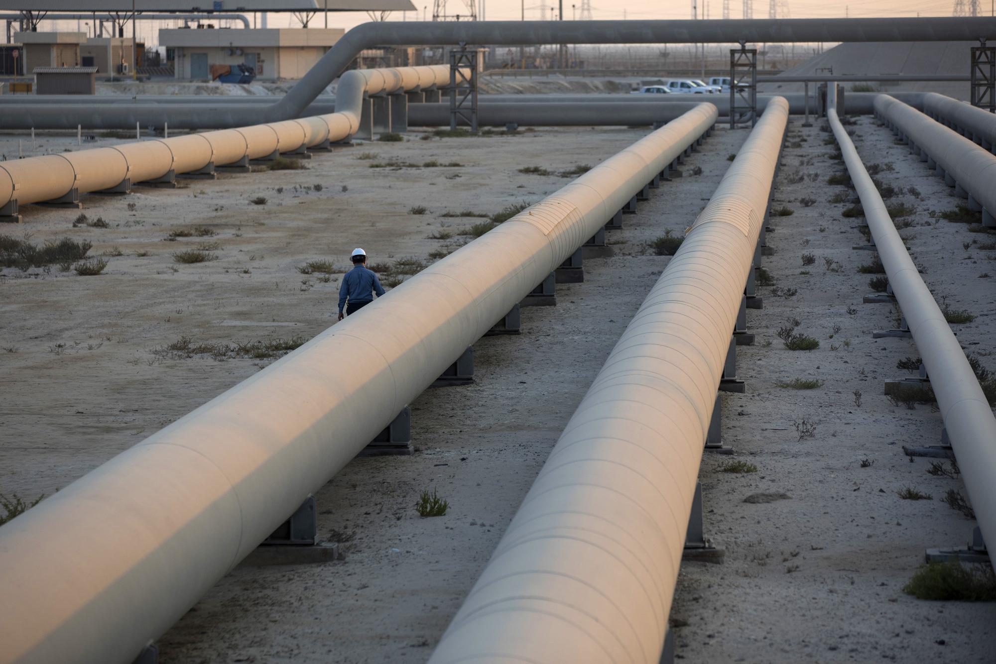 An employee walks along transport pipes leading to oil storage tanks at the Juaymah tank farm at Saudi Aramco's Ras Tanura oil refinery and oil terminal in Ras Tanura, Saudi Arabia.