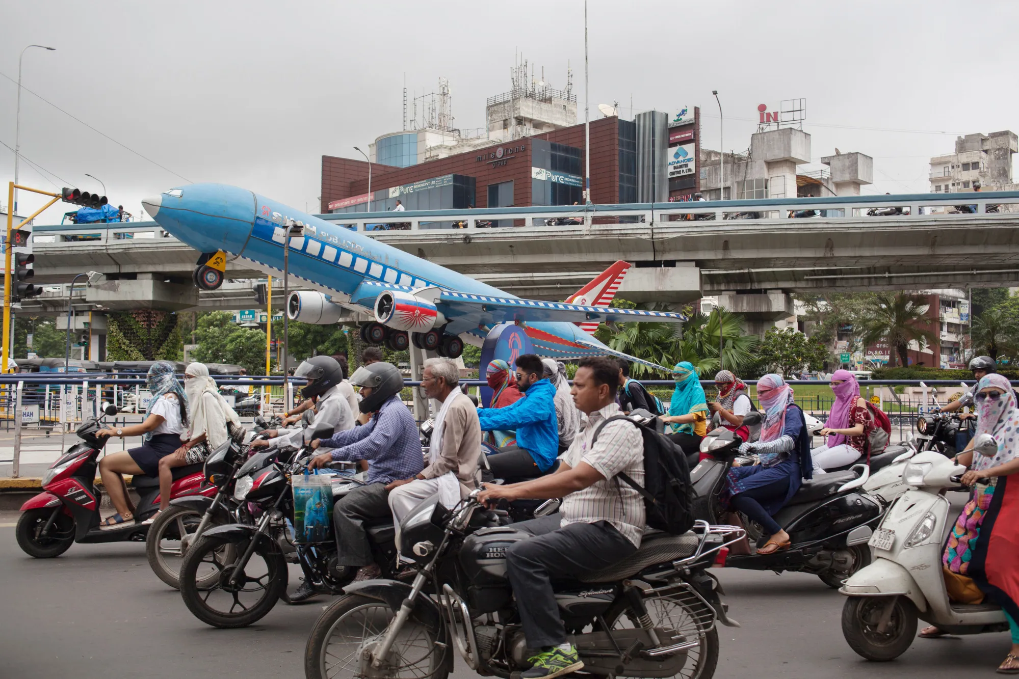 Motorcyclists ride past a model aircraft displayed between highways in Surat, Gujarat, India.