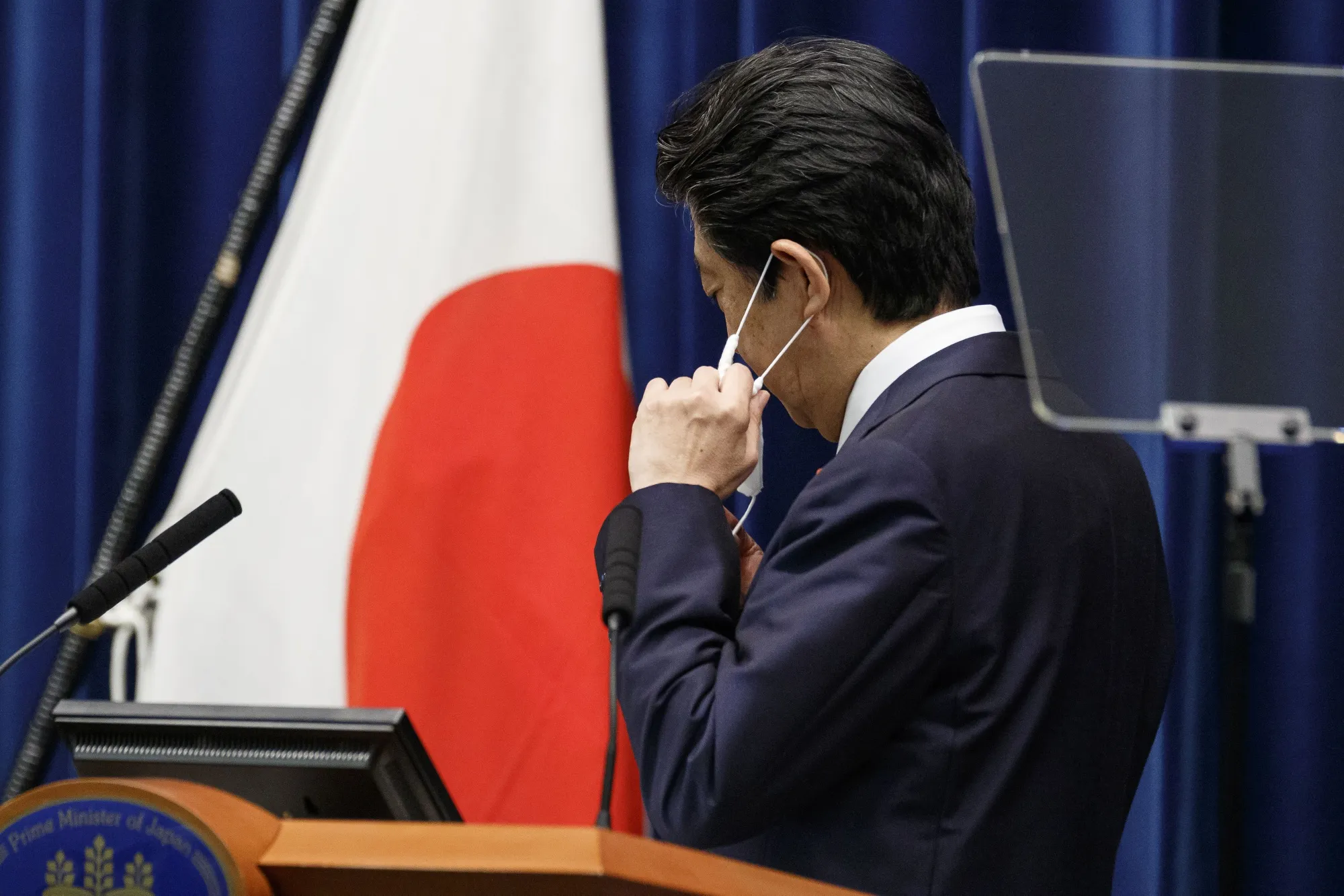 Shinzo Abe removes his face mask at a news conference in June.