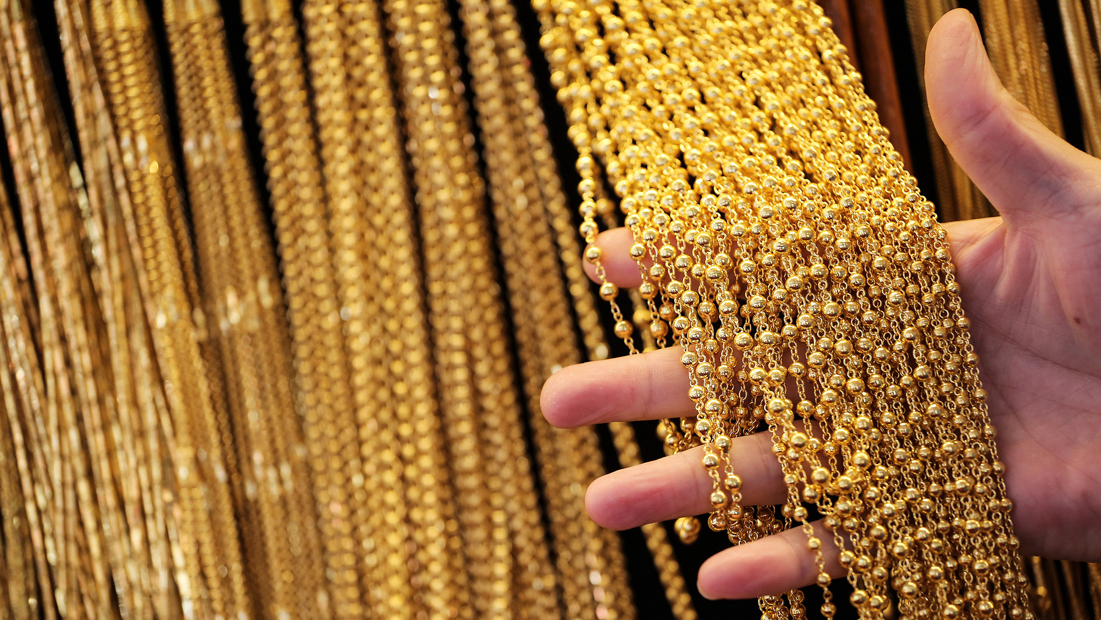 A store assistant handles gold chains hanging from a wall display.
