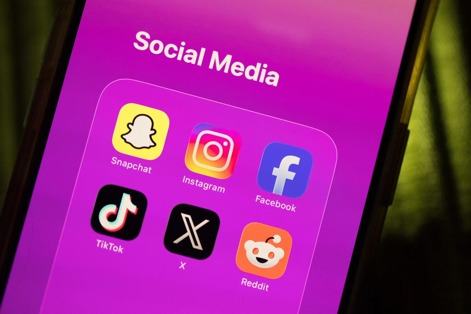 Social media app icons for Snapchat, Instagram, Facebook, TikTok, X and Reddit are displayed on a smartphone.