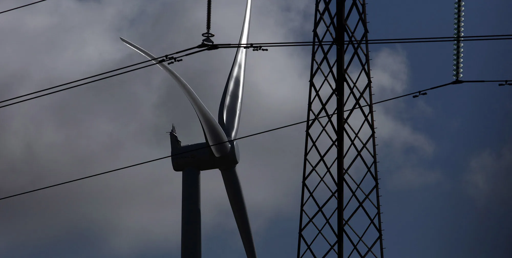 A wind turbine operates near an electricity pylon carrying high tension power lines in Aggersund, Denmark.