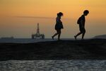 An oil platform floats offshore as people walk on Itacoatiara beach in Niteroi, Brazil, on Friday, Sept. 6, 2013.