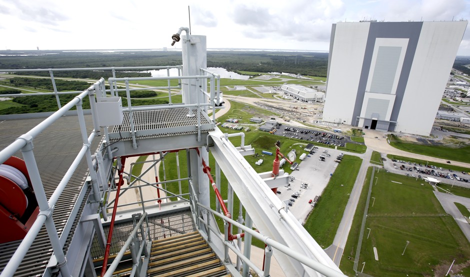A view of the Vehicle Assembly Building, right, is seen from atop the over 400 foot high mobile launcher structure for NASA's Space Launch System.