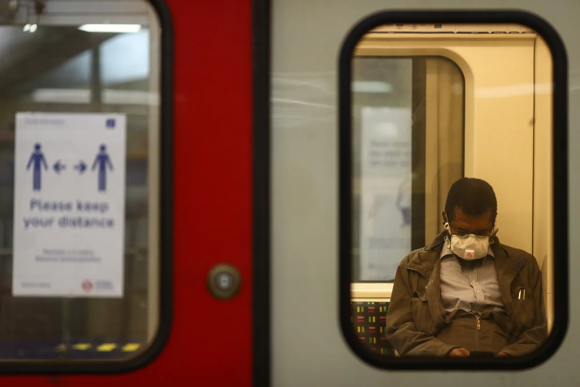A commuter wearing a protective face mask sits on board a London Underground train.