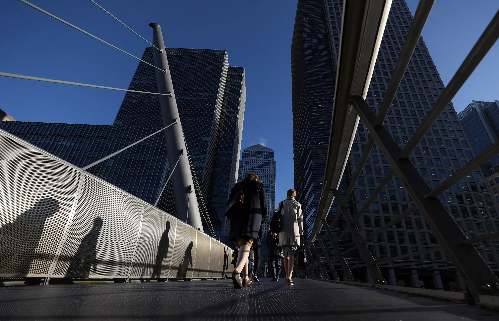 Pedestrians cross a foot bridge towards the offices of global financial institutions, including JPMorgan Chase &amp; Co. and the commercial office block No. 1 Canada Square, in the Canary Wharf financial, shopping and business district in London, U.K., on Tuesday, April 18, 2017.&nbsp;