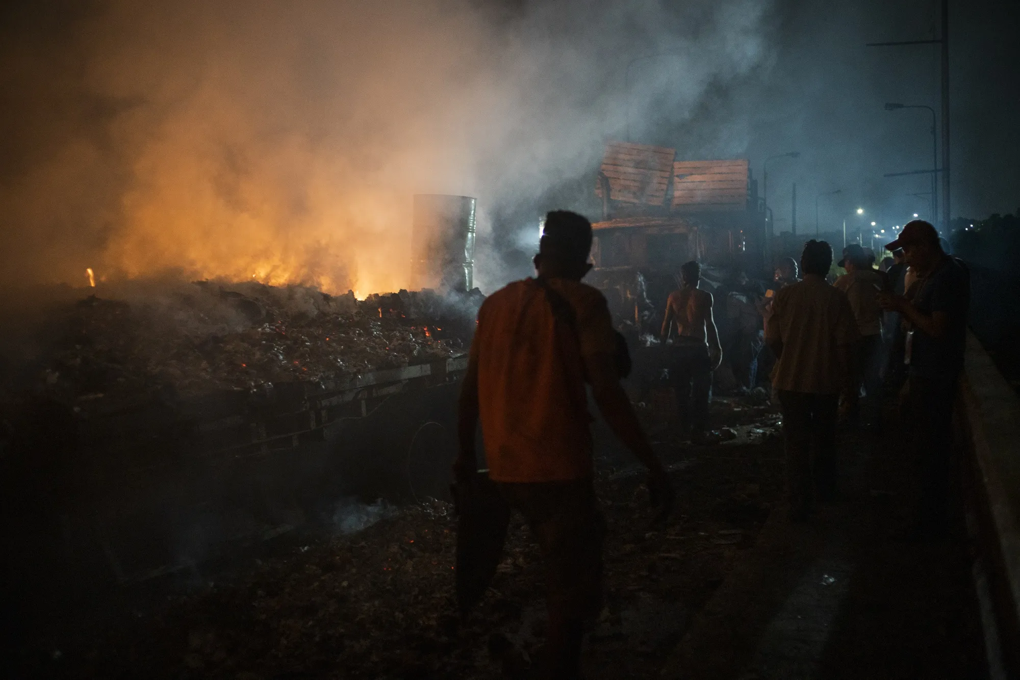 People stand in smoke as a truck previously loaded with humanitarian aid is lit on fire on the Francisco De Paula Santander International Bridge near the border with Venezuela in Cucuta, Colombia.