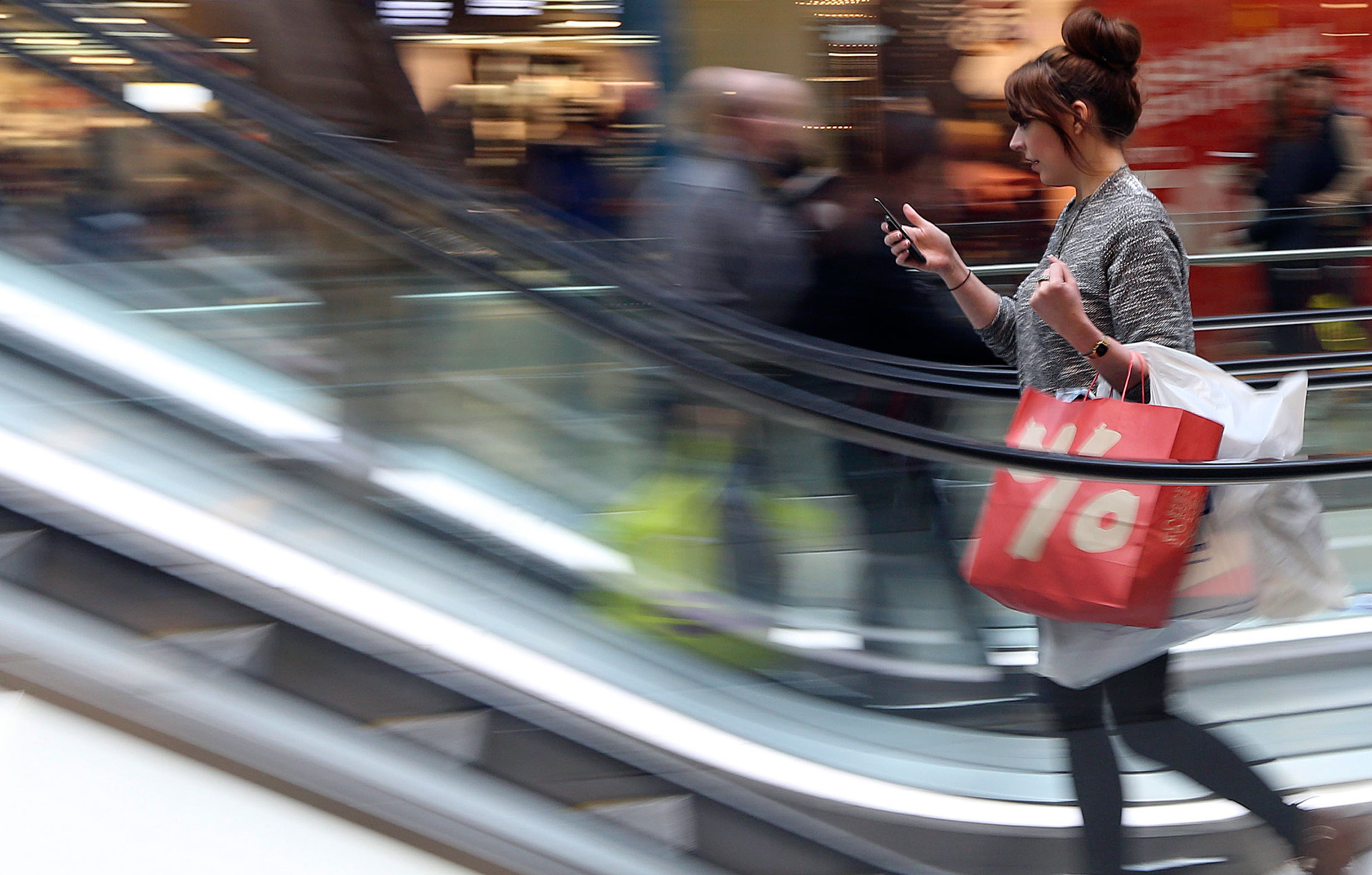 A shopper checks her mobile phone as she stands on an escalator at the Westfield Stratford City shopping mall in London, U.K., on Thursday, Dec. 27, 2012.
