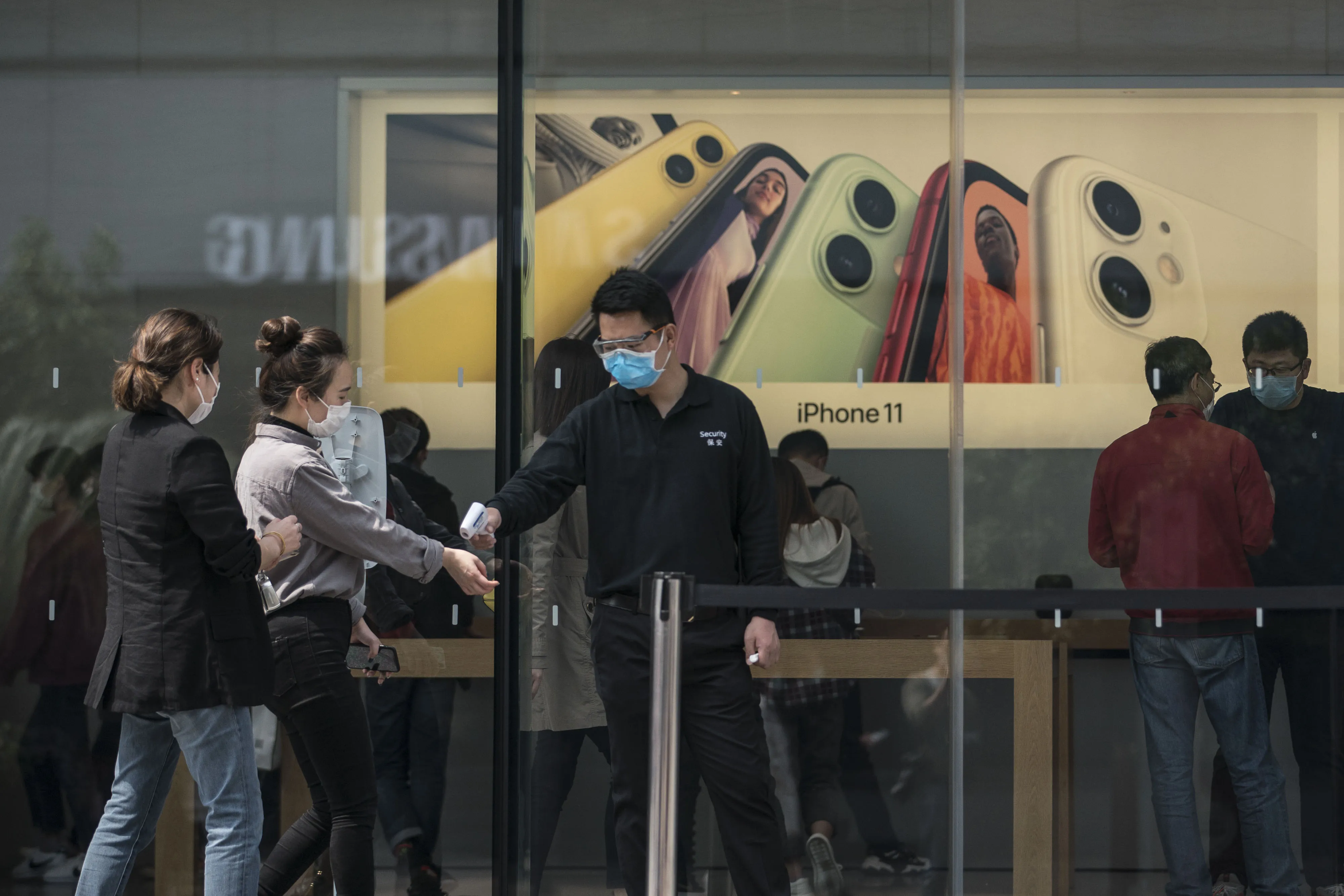 An employee wearing a protective mask checks the temperature of customers outside an Apple Inc. store in Shanghai.