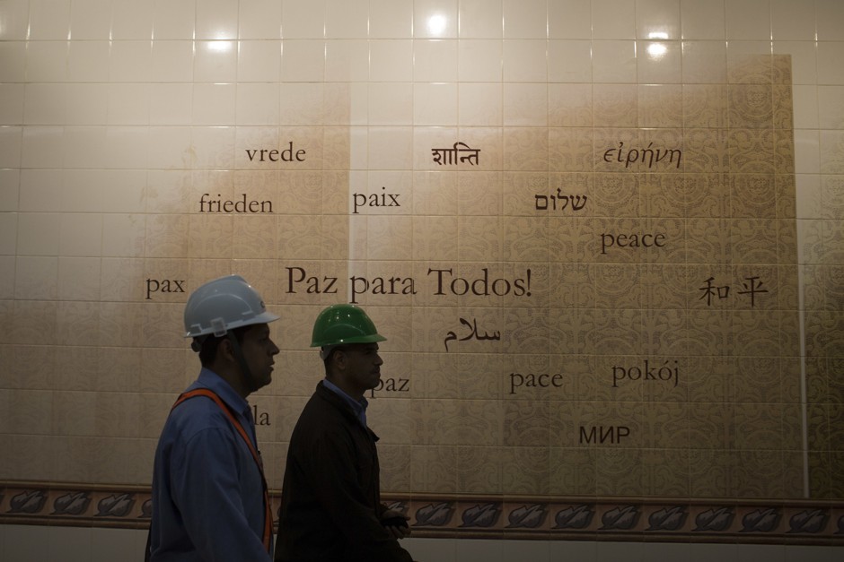 Workers walk past a mural on the new subway station at Ipanema.