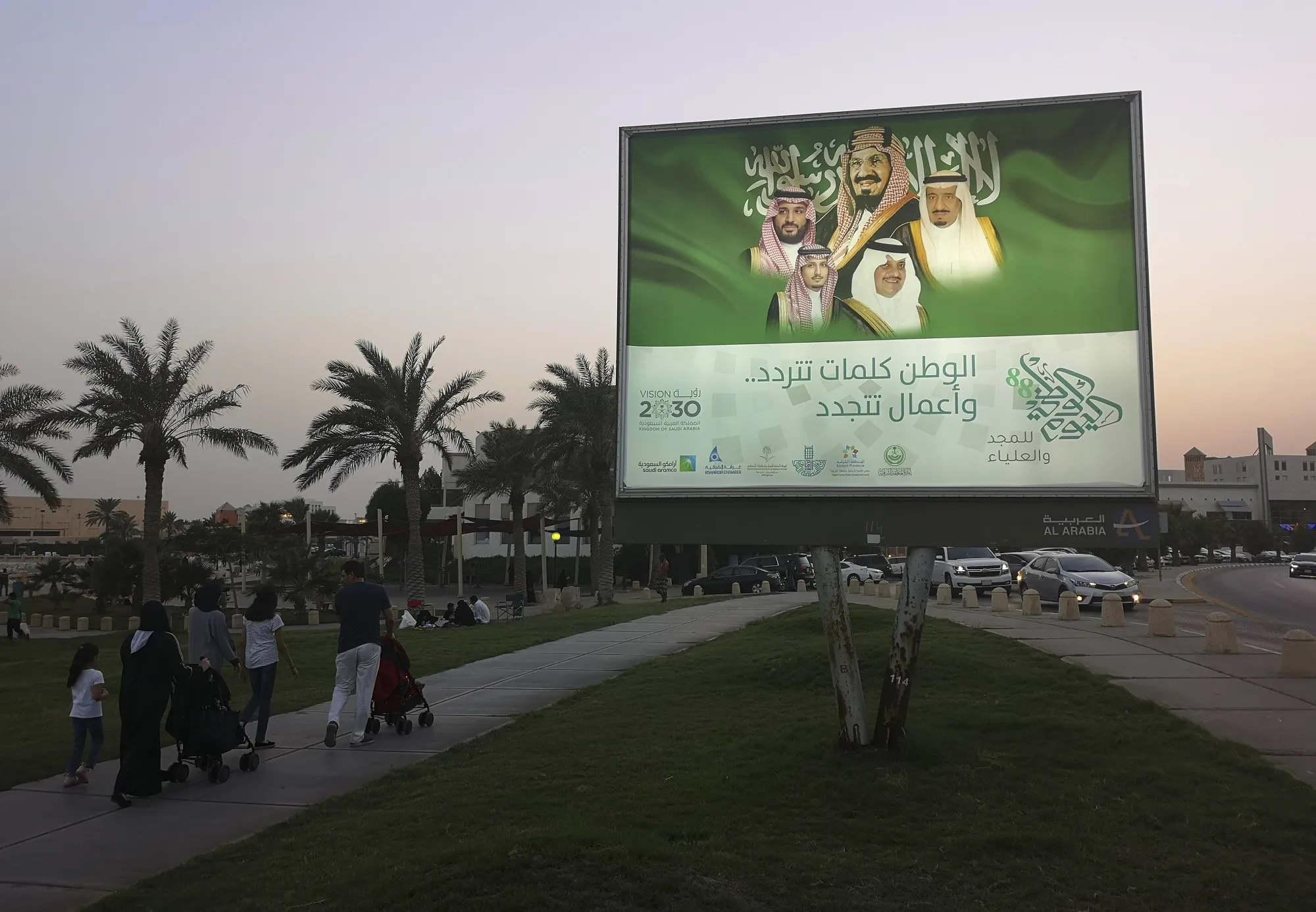 Pedestrians walk past an illuminated sign&nbsp;showing portraits of the Saudi Arabian Royal family in Dhahran, Saudi Arabia.