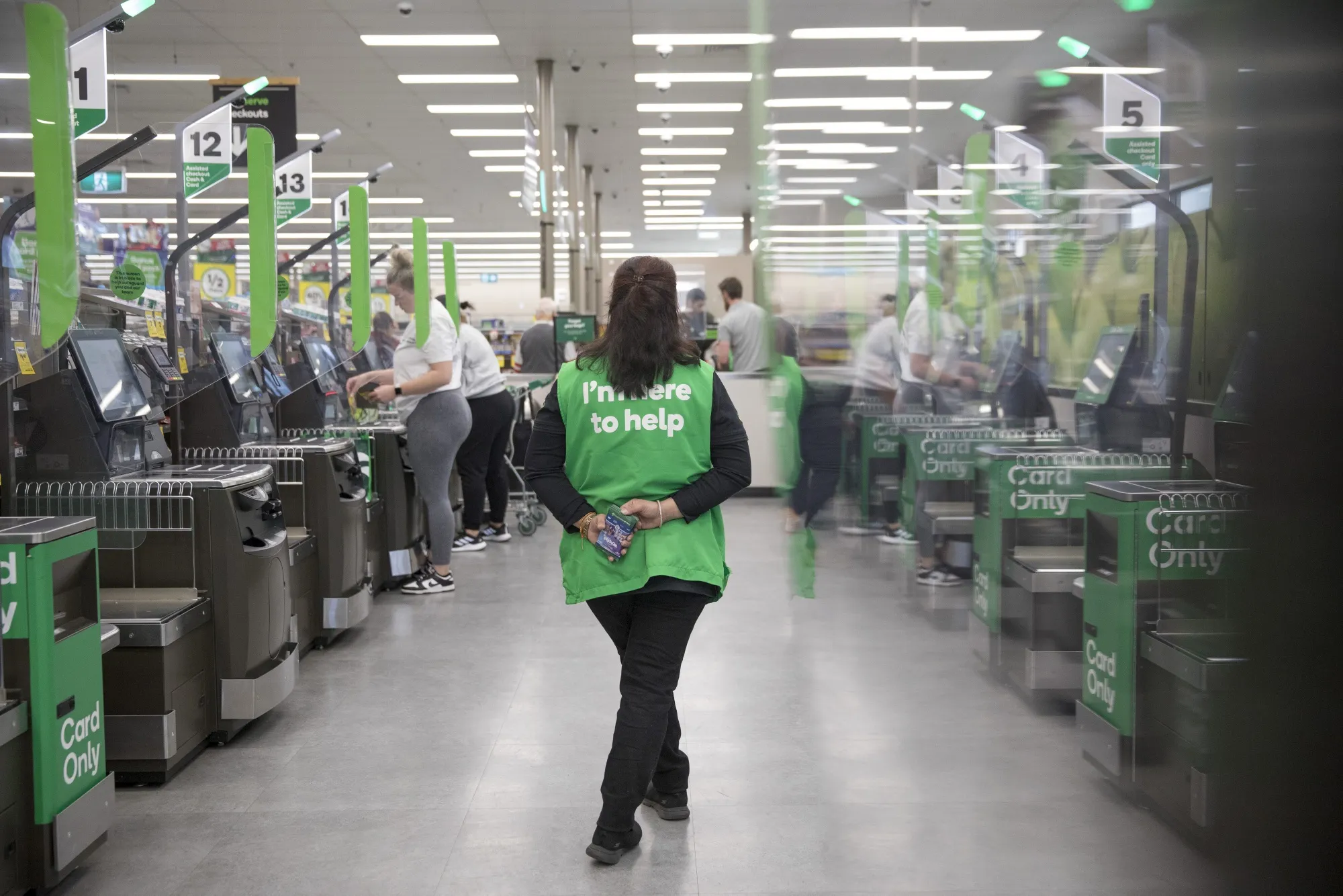 An employee supervises self-service checkout kiosks at a Woolworths Group&nbsp;grocery store in Sydney, Australia.