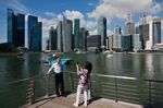 Tourists pose against the Central Business District skyline in Singapore, on Tuesday, Feb. 28, 2012.
