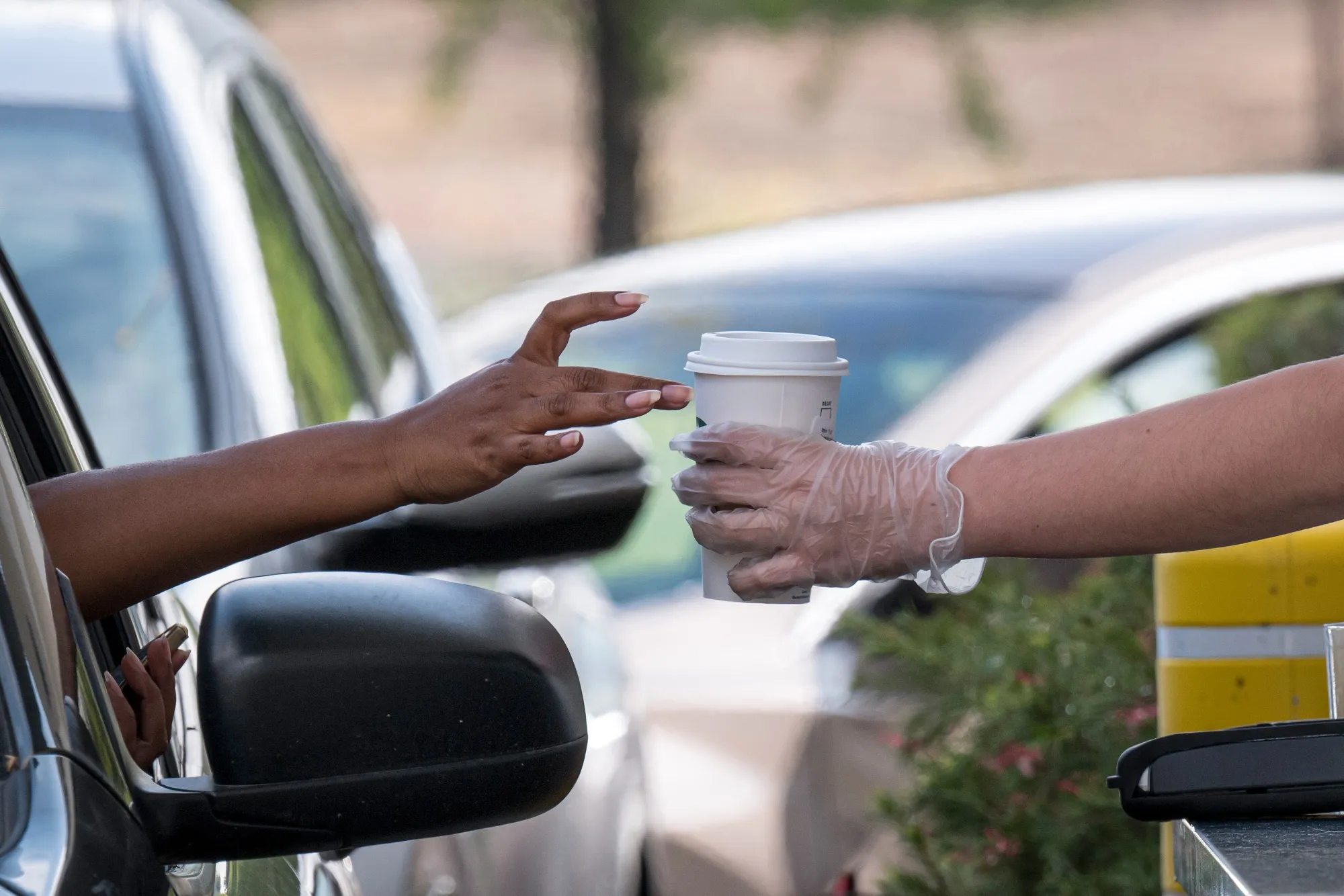 A Starbucks Corp. employee wearing protective gloves hands a customer an order from a drive-thru window at a store in Hercules, California, on April 7, 2020.&nbsp;