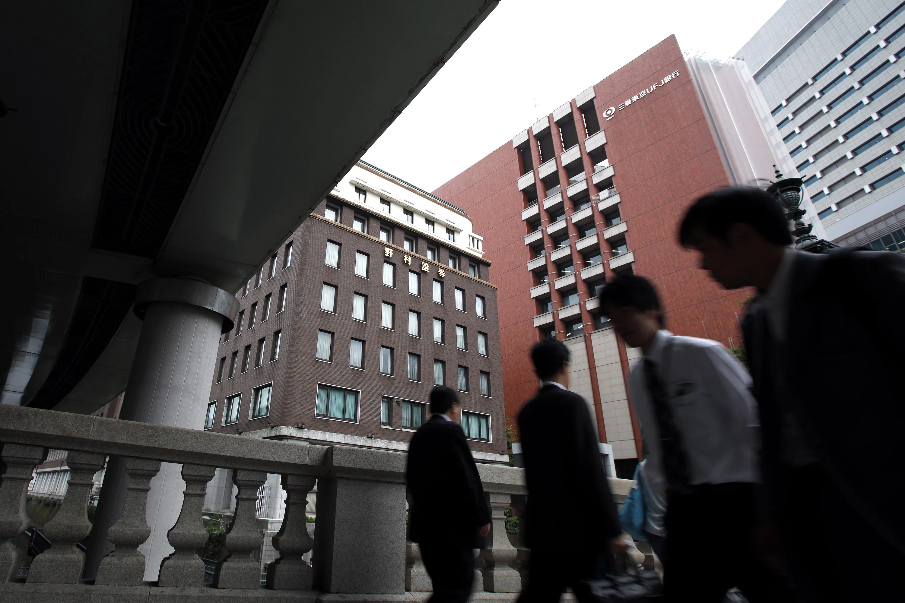 Pedestrians walk past the Nomura Holdings Inc. headquarters, left, in Tokyo.