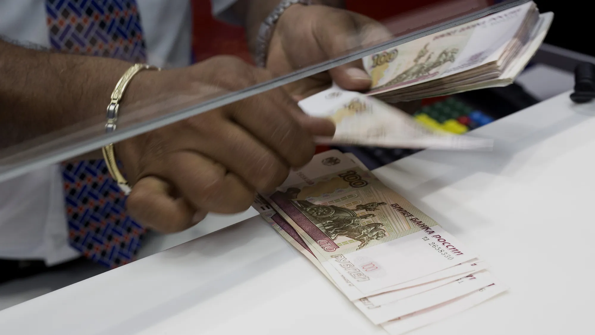 An employee counts one hundred Russian Ruble notes onto a counter.
